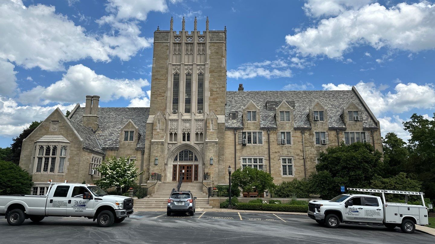 Historic Gothic stone building restored by Alex Restoration, with company trucks on site