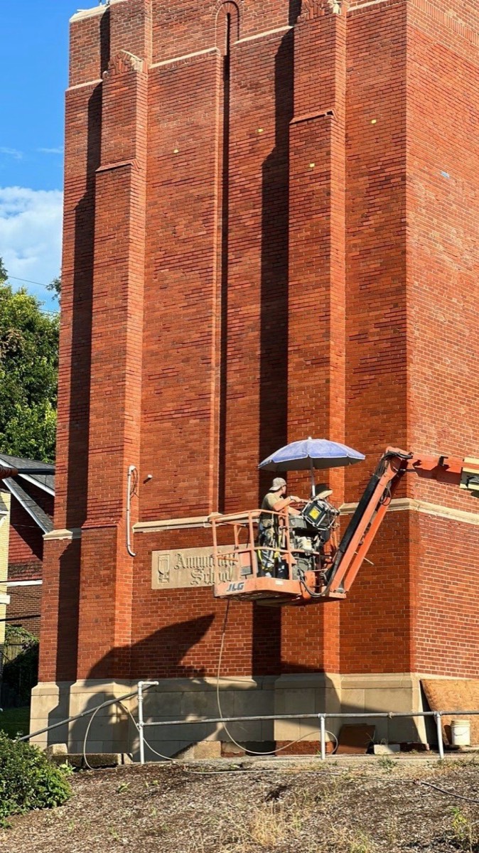 Masons on a lift repointing a tall brick school tower